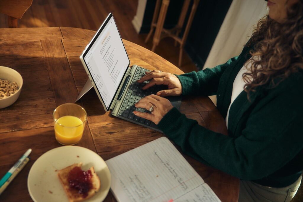 Woman typing on laptop at wooden table with breakfast.