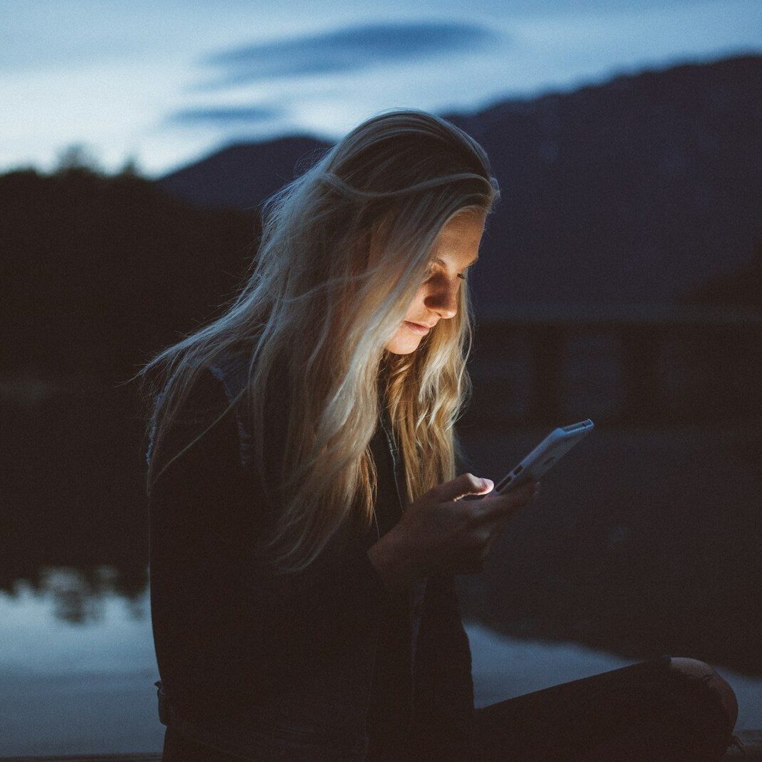 woman looking at phone beside body of water